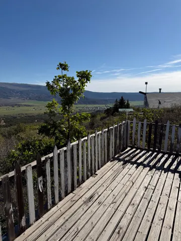 Wood-plank outdoor decking with a picket fence, surrounded by lush foliage and distant mountains