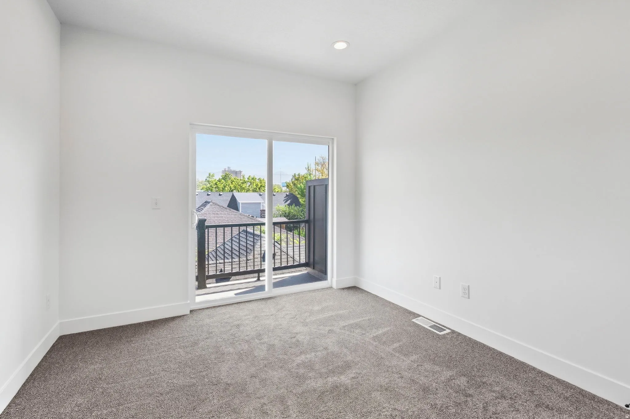 Sliding glass door leading to a balcony with black metal railings, recessed ceiling lighting, and neutral carpet flooring