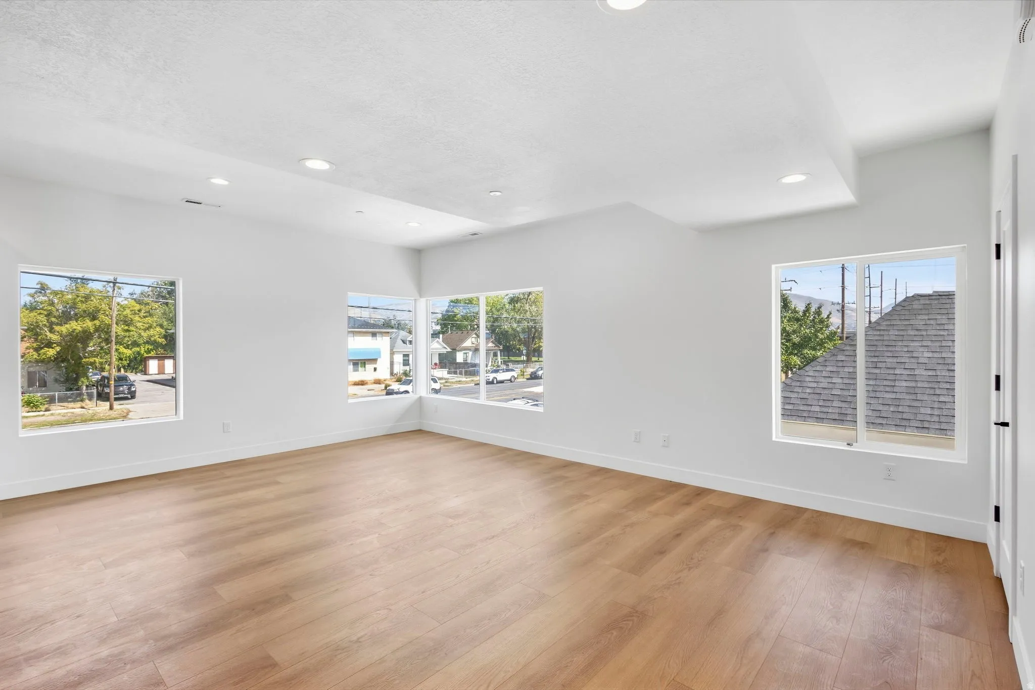 Spacious room featuring wood-finish flooring, recessed lighting, multiple windows, and a vaulted ceiling