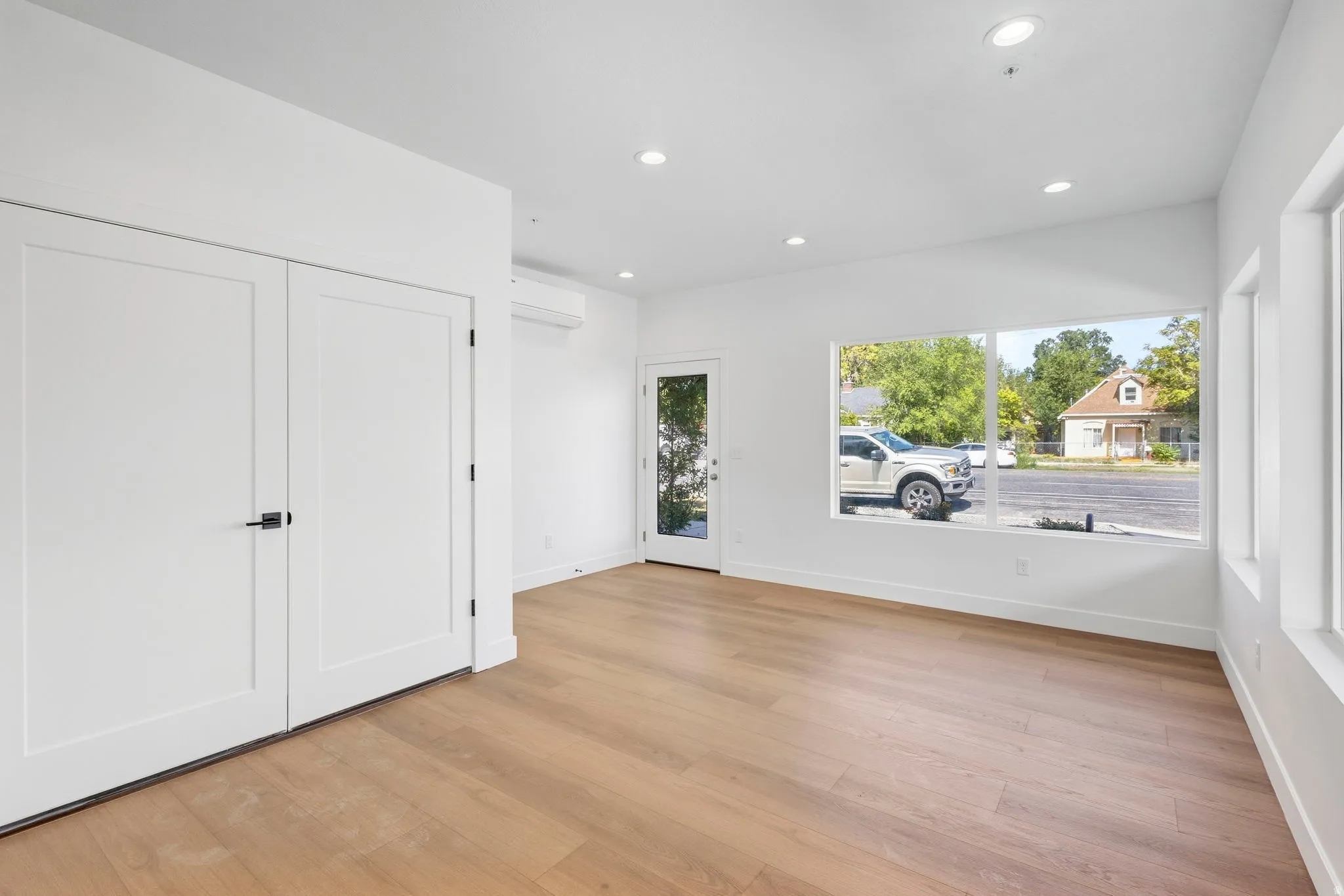 Recessed lighting, wood-finish flooring, white flat-panel doors with matte black hardware, large windows, and a glass-paneled exterior door