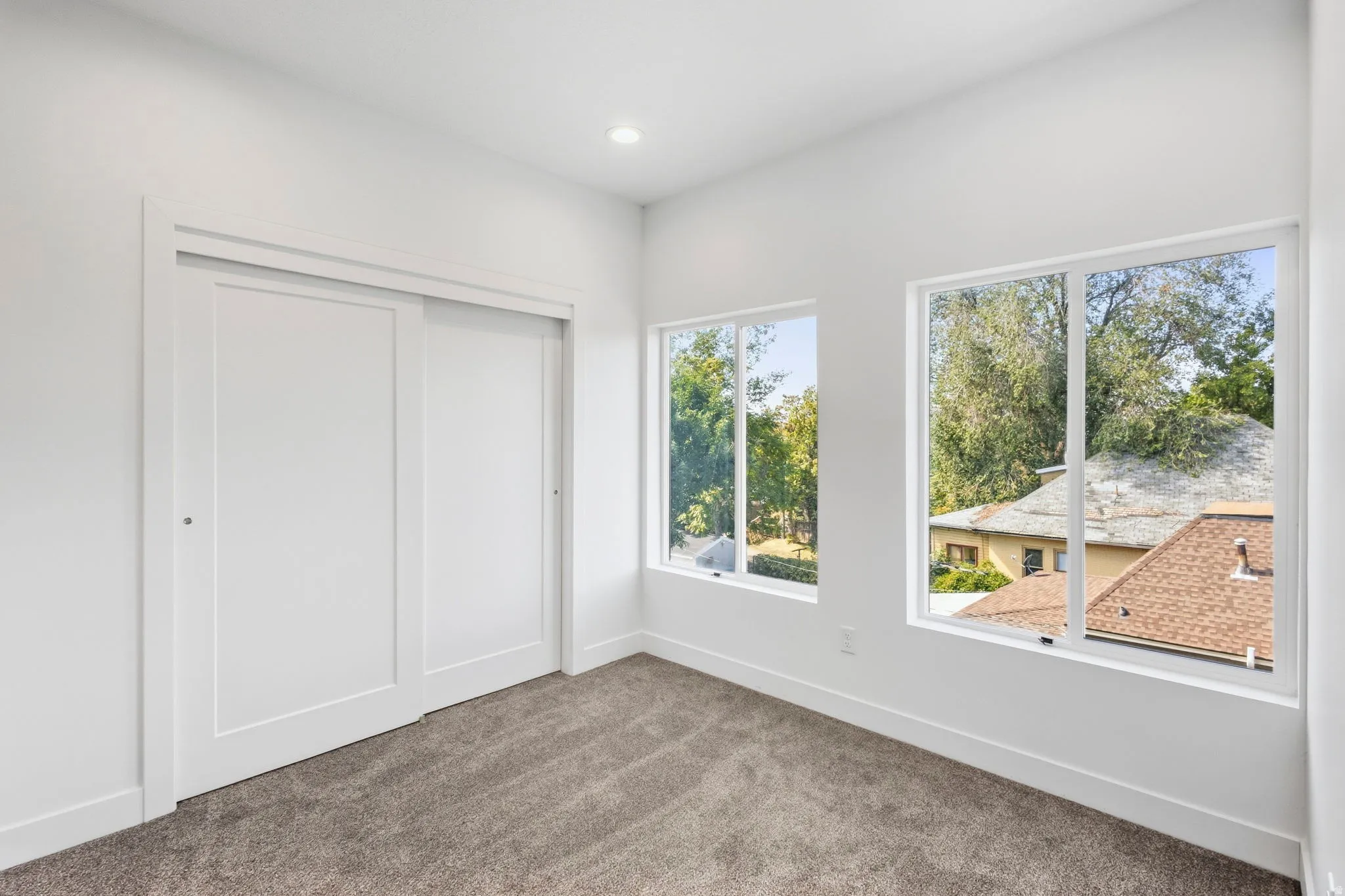 Recessed lighting, white walls, two large windows, carpet flooring, and a sliding closet door
