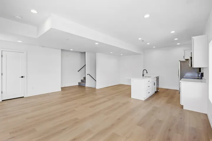 Open-concept living space with wood-finish flooring, recessed lighting, a white kitchen island with an integrated sink, and white cabinetry