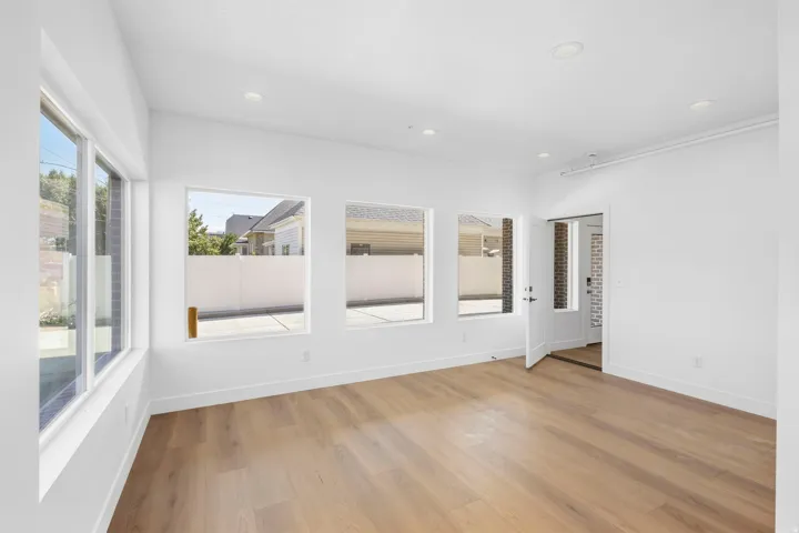 Recessed lighting, wood-finish flooring, white walls, multiple windows, and a white door with dark hardware