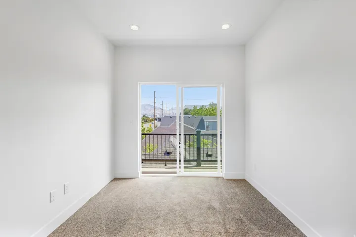 Sliding glass door leading to a balcony with metal railing, recessed ceiling lighting, and neutral carpeting