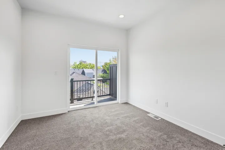 Sliding glass door leading to a balcony with black metal railings, recessed ceiling lighting, and neutral carpet flooring