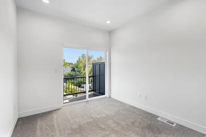 Carpeted room with recessed lighting and a sliding glass door leading to a balcony with black metal railings
