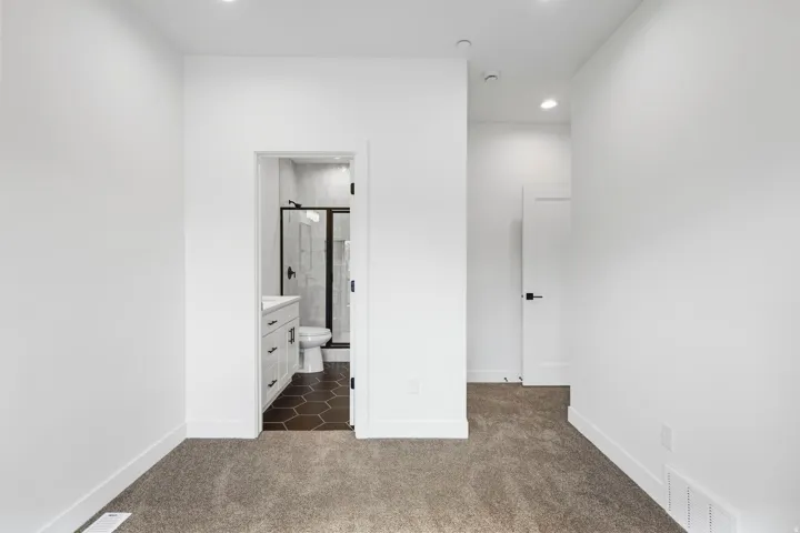 Carpeted room with recessed lighting and a white door featuring a black handle