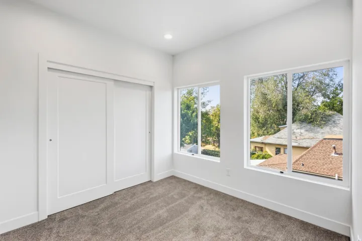 Recessed lighting, white walls, two large windows, carpet flooring, and a sliding closet door