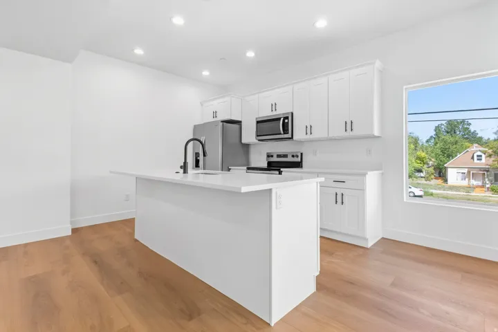 Kitchen featuring wood-finish flooring, white cabinetry, stainless steel appliances, a center island with a sink, and recessed lighting