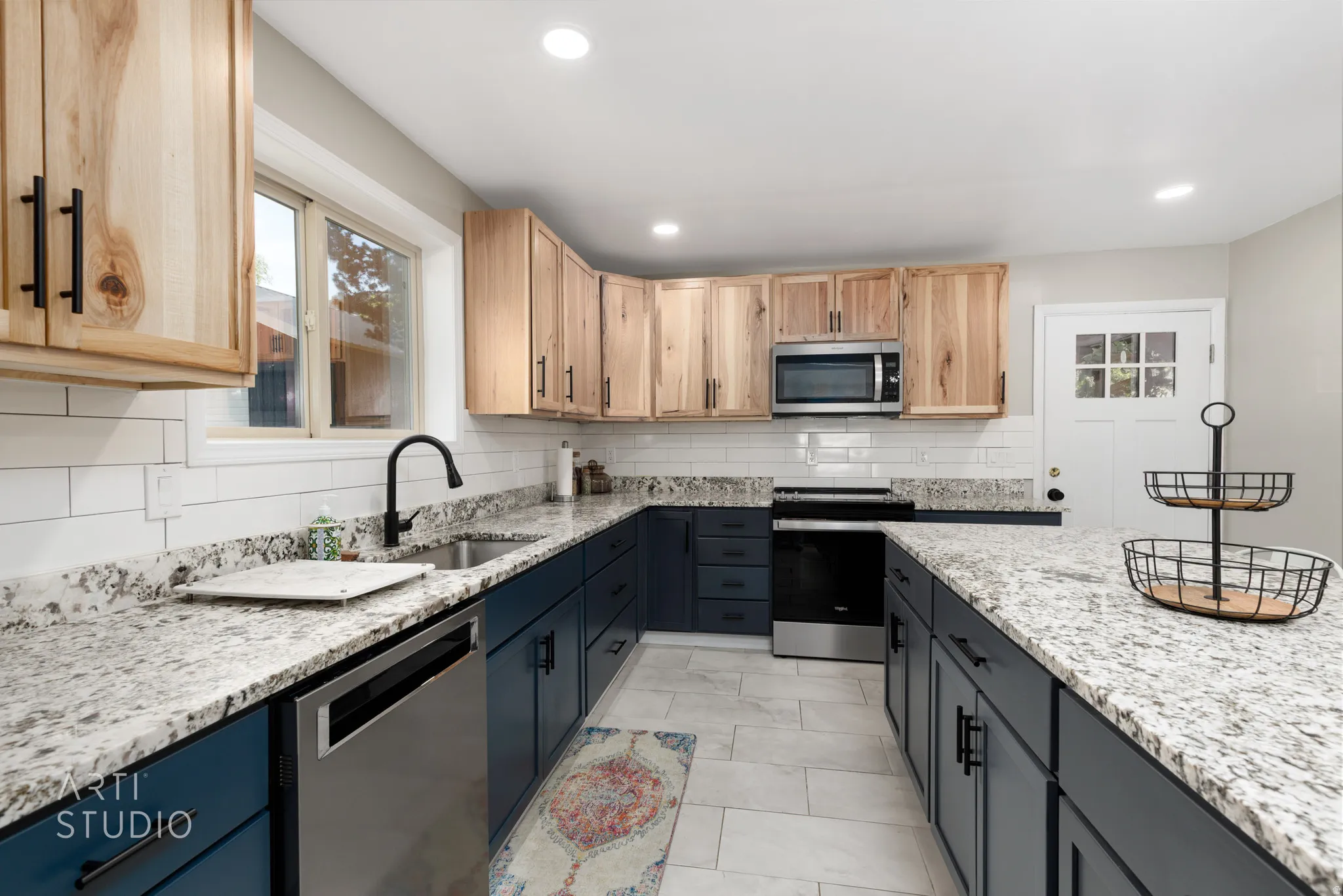 Kitchen featuring natural wood-finish upper cabinetry, blue lower cabinetry, stone countertops, white subway tile backsplash, and stainless steel appliances