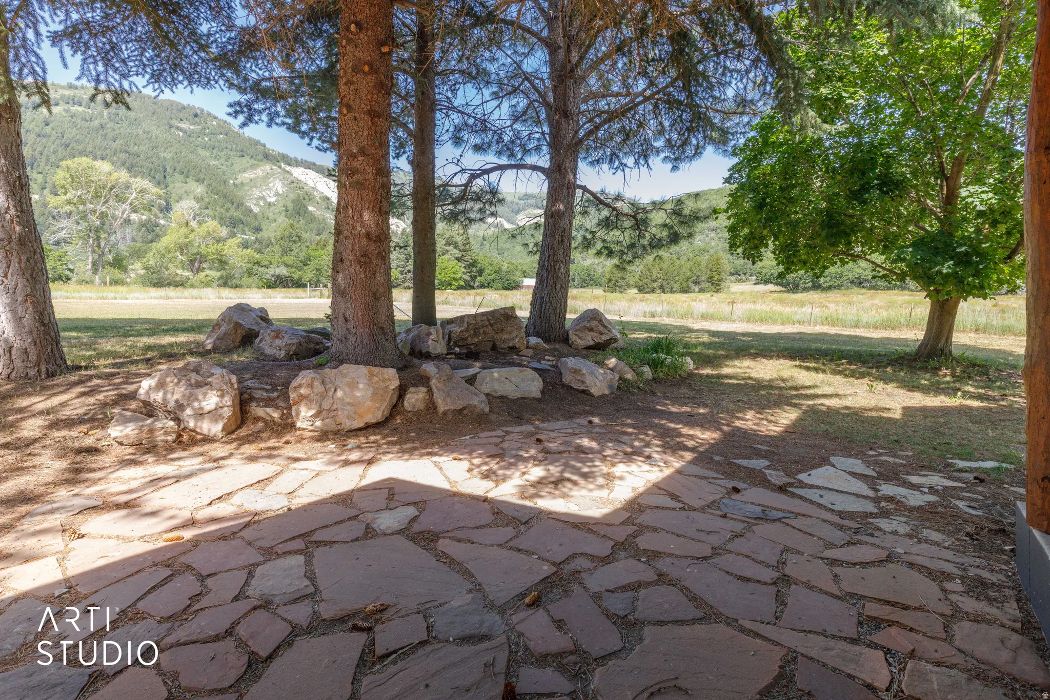 Natural stone patio with irregular flagstone, surrounded by mature trees, and a distant mountain backdrop