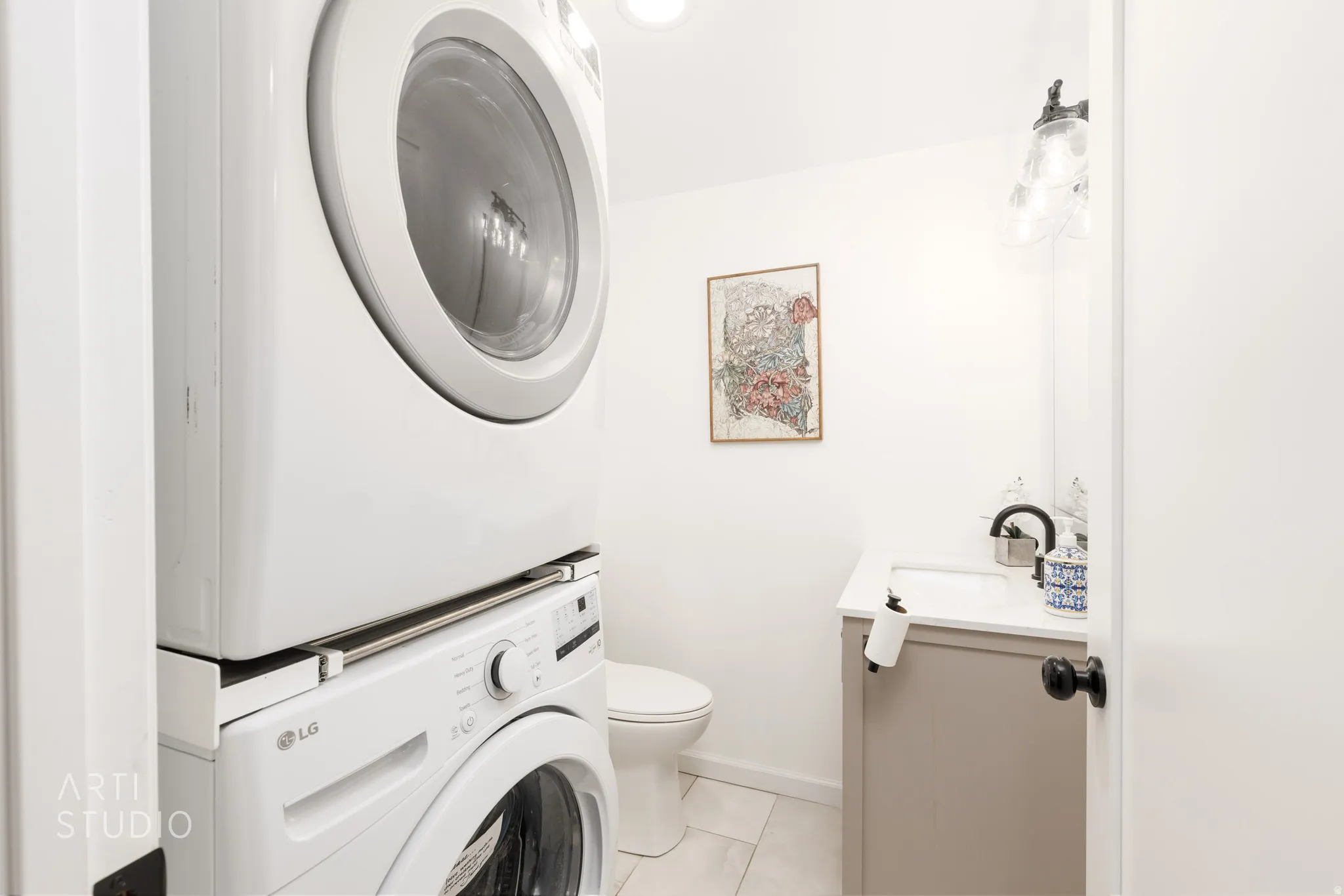 Stackable washer and dryer, vanity with a white countertop, wall-mounted light fixture, and toilet