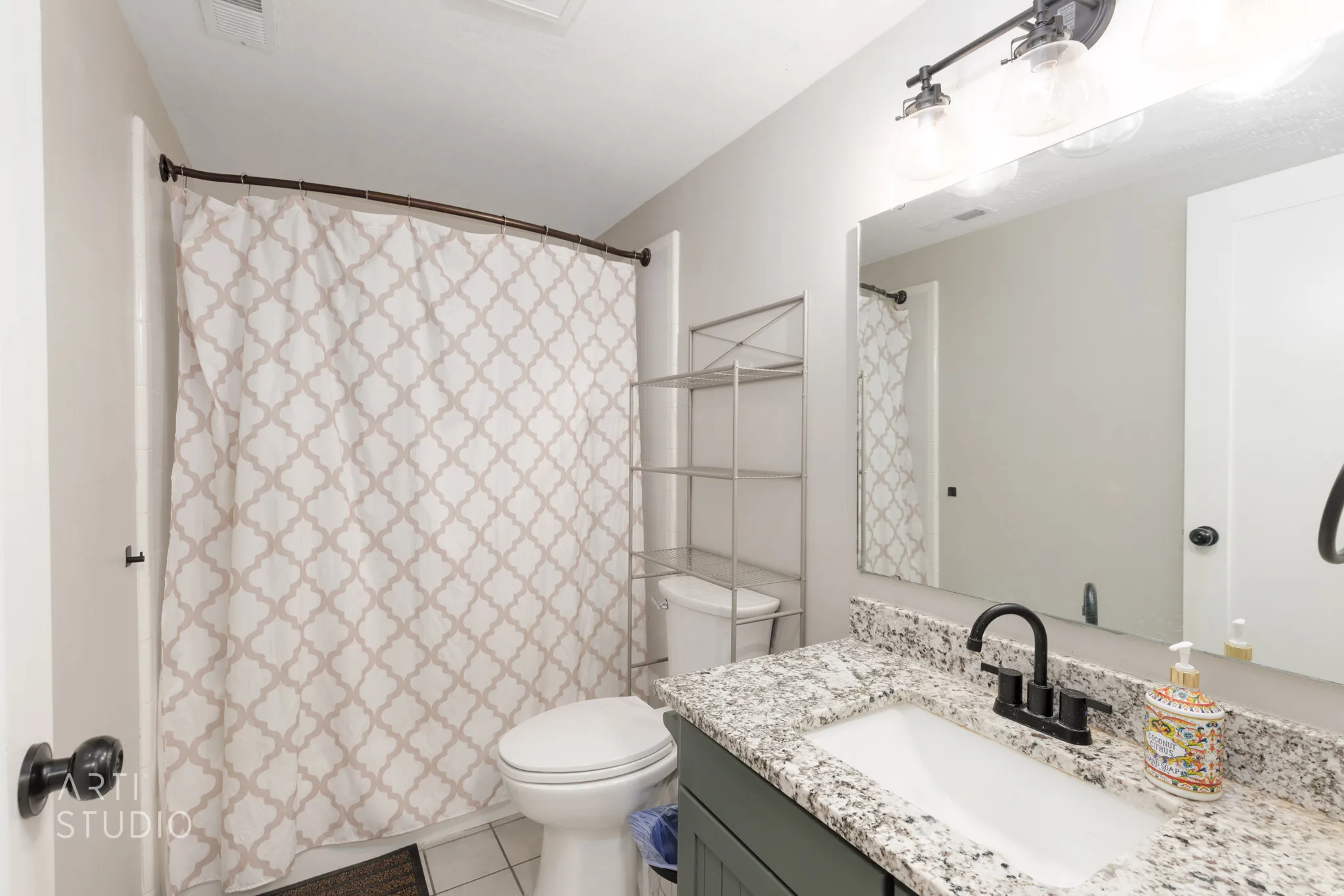 Bathroom featuring a vanity with a white rectangular sink, granite-style countertop, matte black faucet, and a wall-mounted mirror with an overhead light fixture