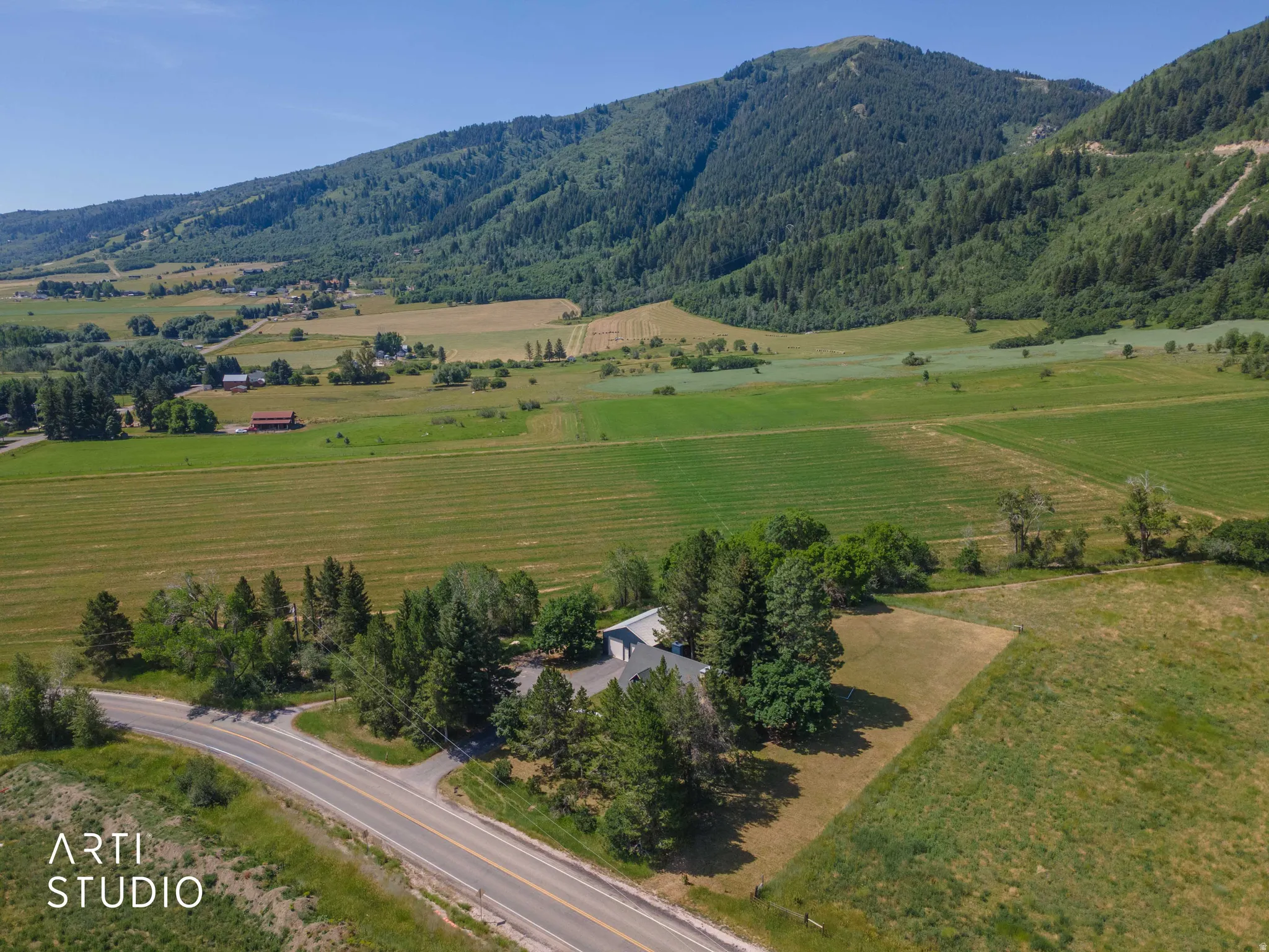 Expansive rural property featuring a single-story residence, mature trees, and a paved road frontage