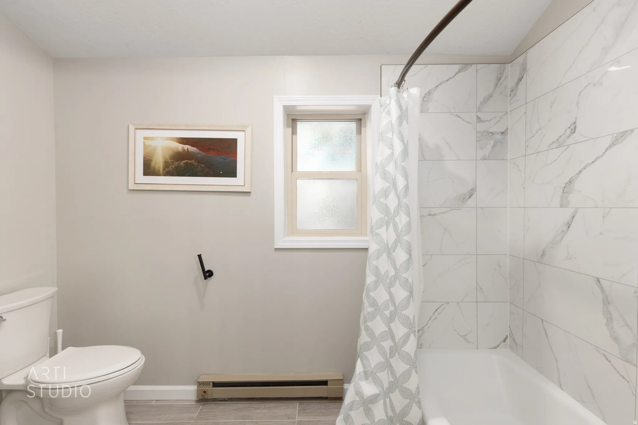 Bathtub with white subway tile surround featuring gray veining, white toilet, and a window with frosted glass
