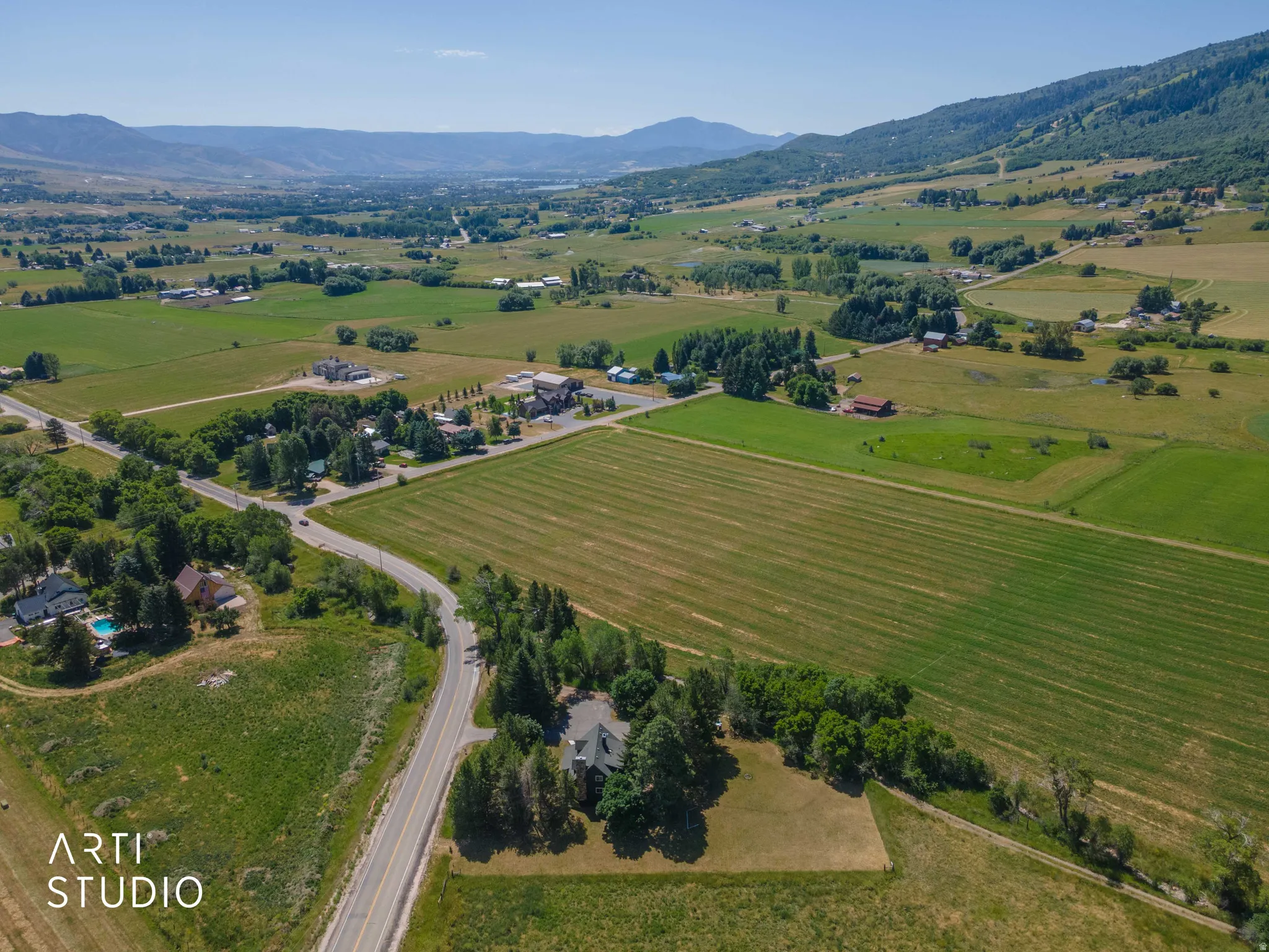 Expansive rural setting featuring a winding road, lush green fields, and distant mountains