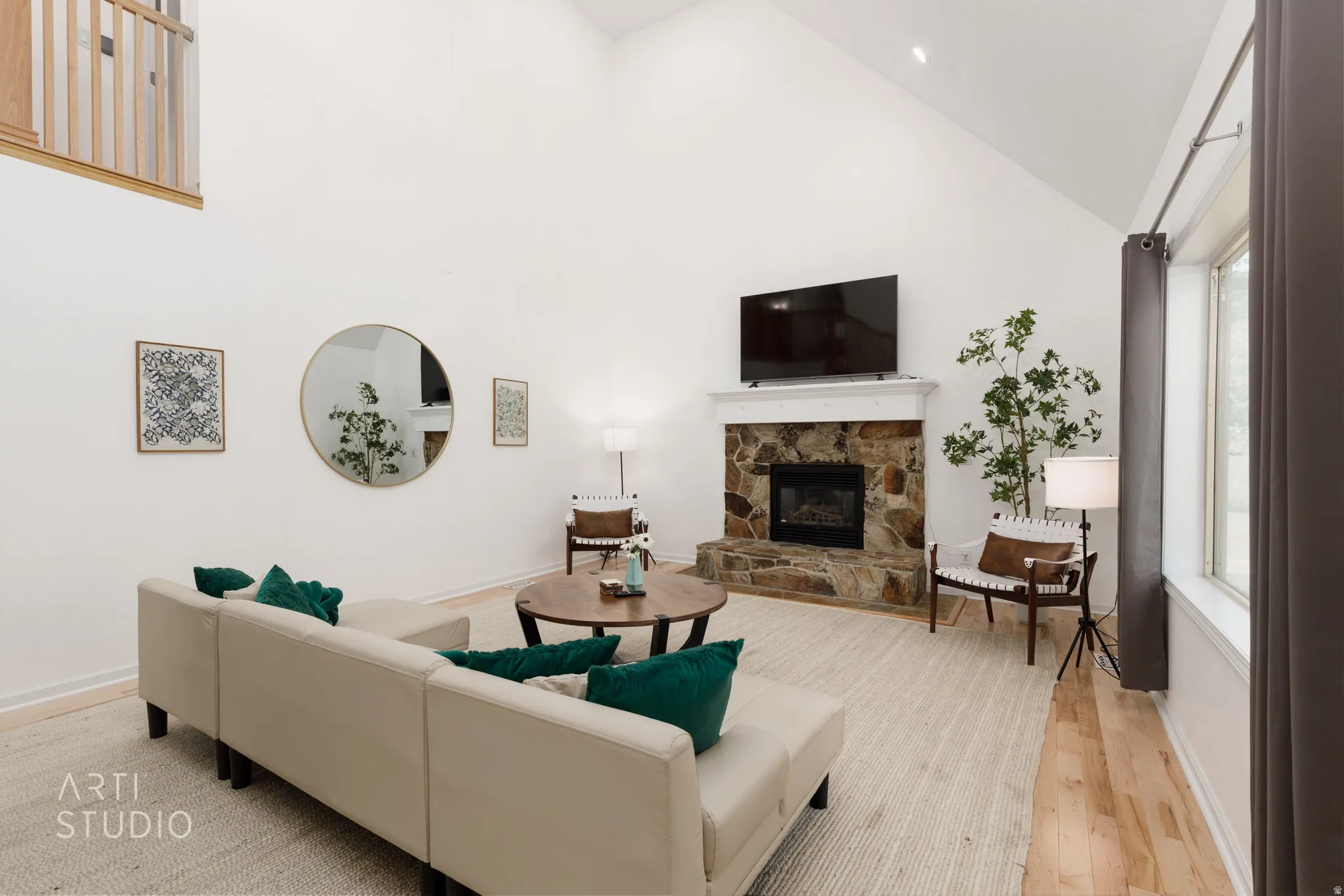 Vaulted ceiling, stone-faced fireplace with white mantle, wood-finish flooring, large window, and an interior balcony
