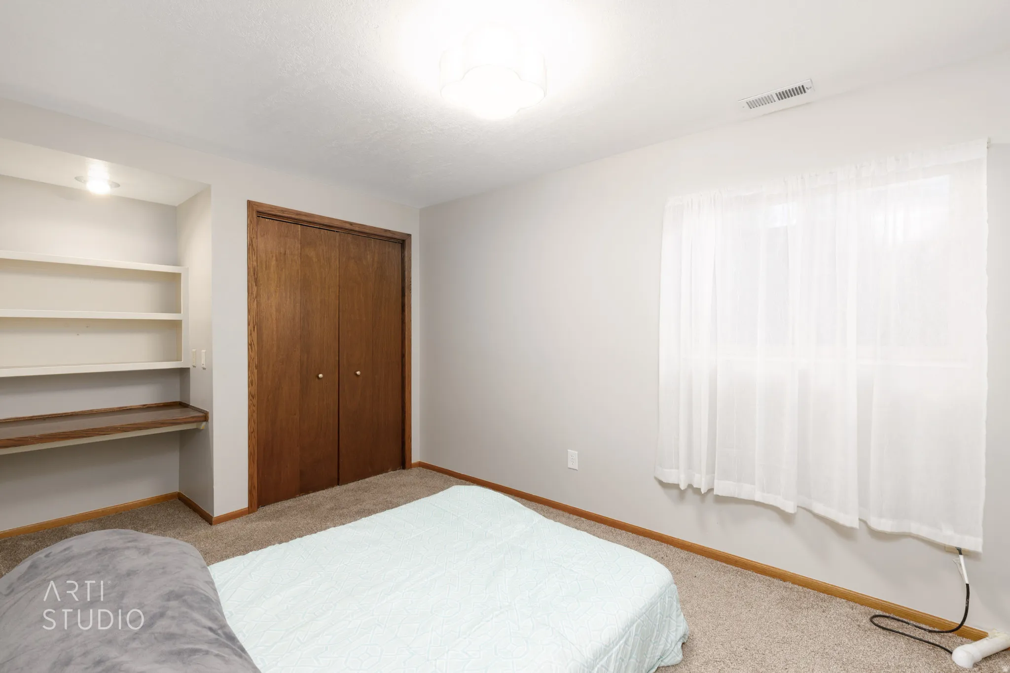 Built-in shelving with integrated desk, wood-panel bi-fold closet doors, wall-to-wall carpeting, and a flush-mount ceiling light fixture