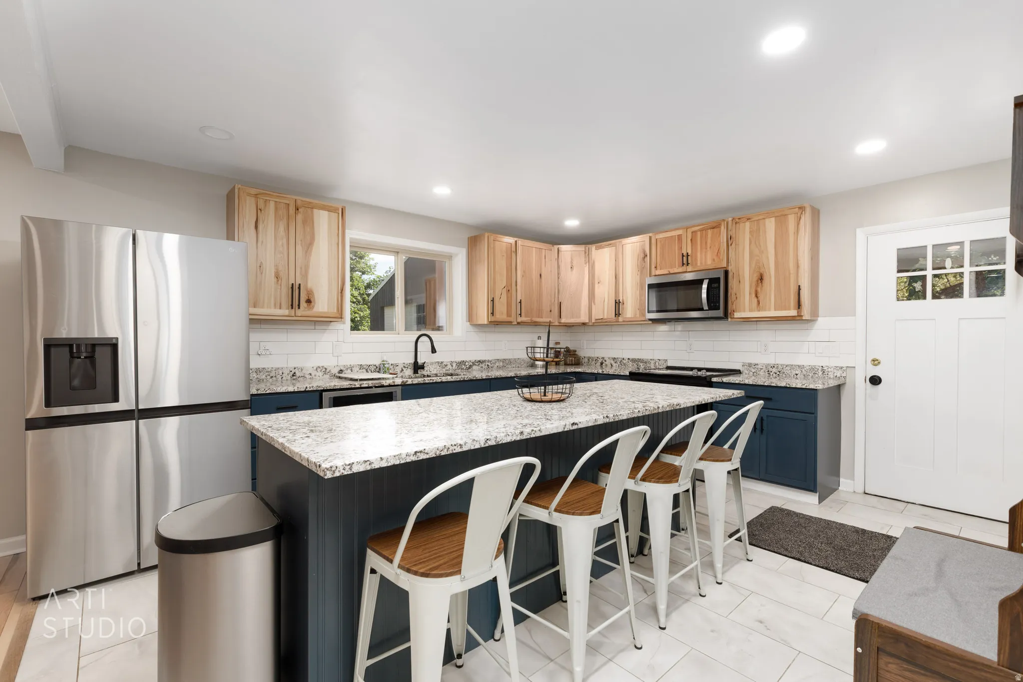 Kitchen featuring a large island with a stone-finish countertop, light wood-finish cabinetry, stainless steel appliances, a white subway tile backsplash, and light tile flooring