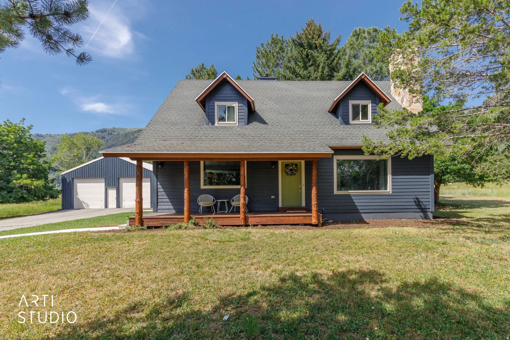 Siding exterior with dormer windows, covered front porch with wood-finish columns, and a two-car detached garage with a separate entry