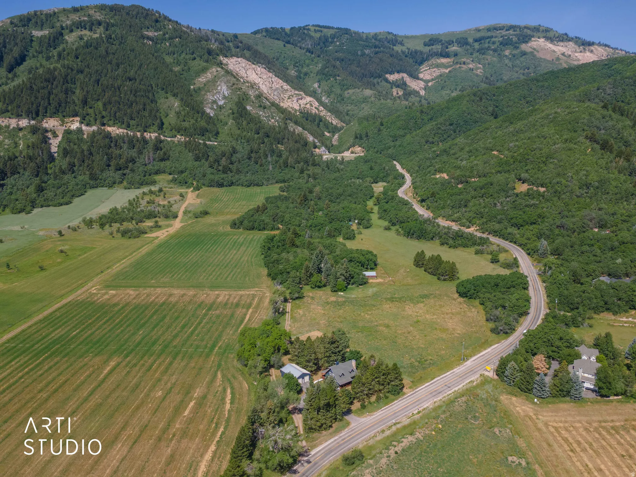 Expansive landscape with a winding paved road, agricultural fields, and a mountainous backdrop