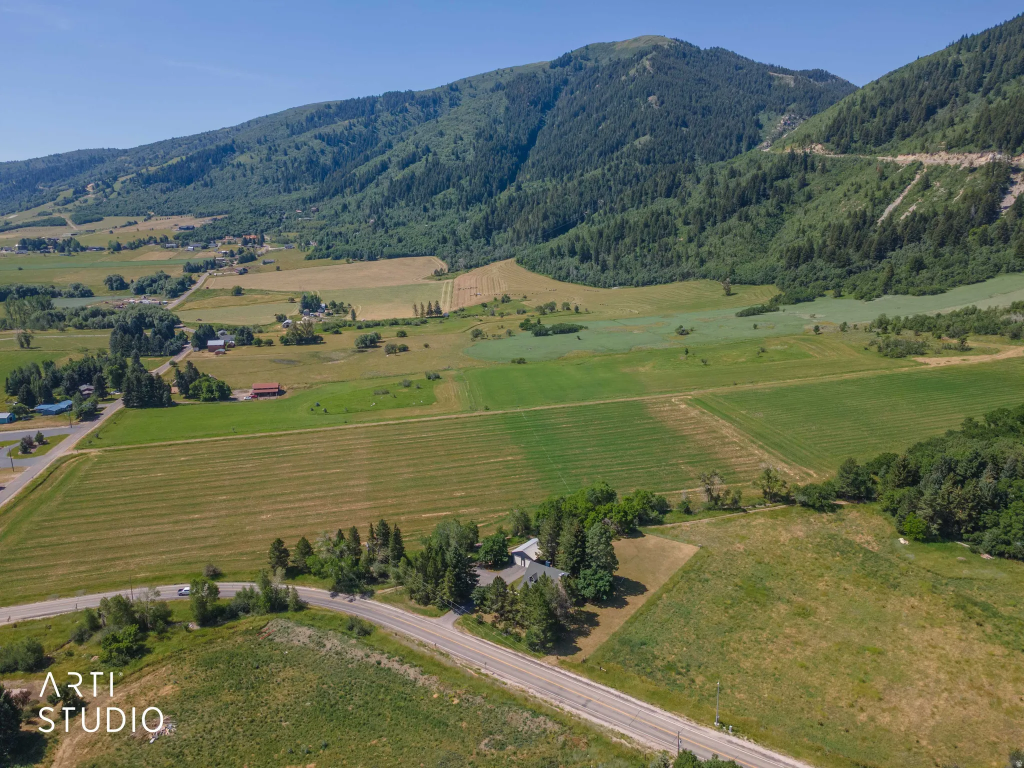 Expansive property featuring verdant fields, a mountainous backdrop, and a paved roadway