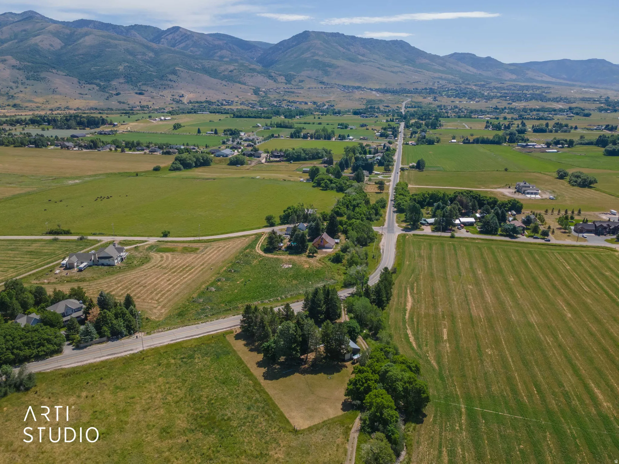 Expansive rural landscape featuring distant mountains, open fields, scattered residential structures, and paved roads