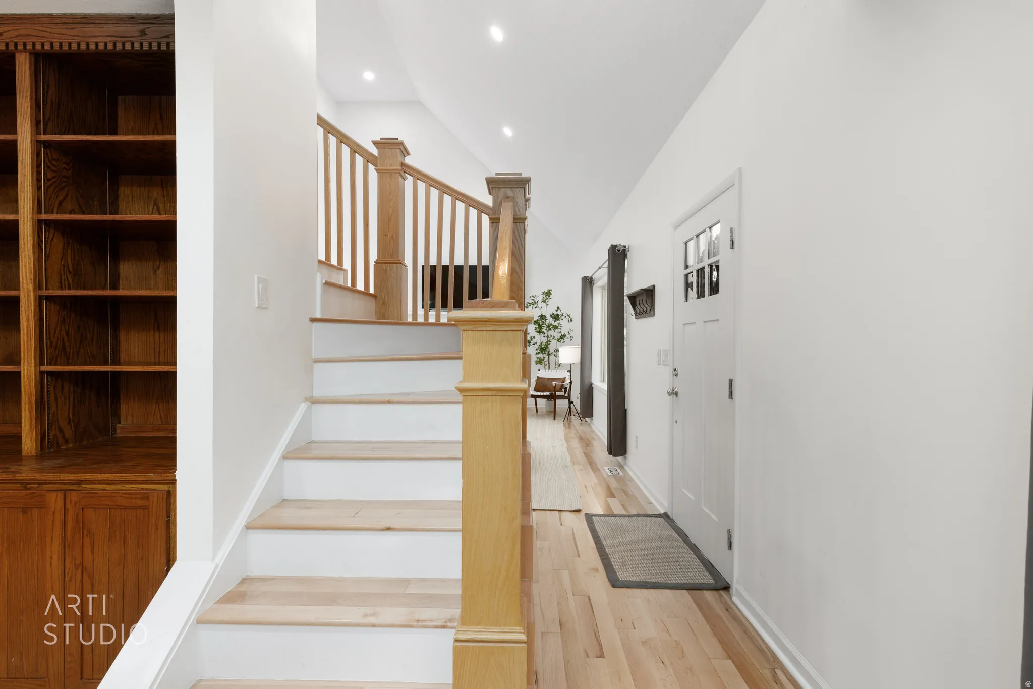 Hardwood flooring, painted white walls, recessed ceiling lighting, built-in wooden shelving, and a wooden staircase with white risers