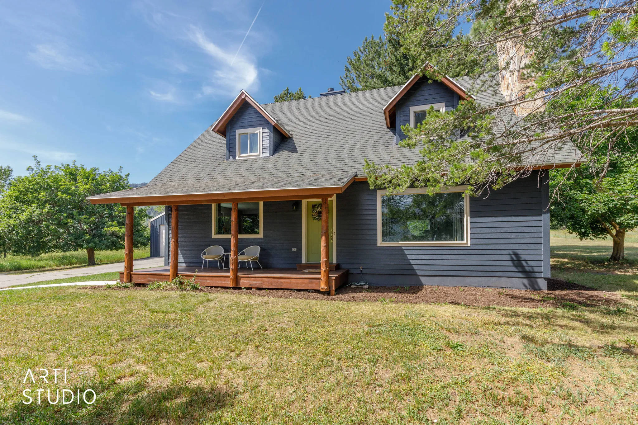 Charcoal-colored siding with a light green front door, covered porch with natural wood pillars, and a grey shingle roof