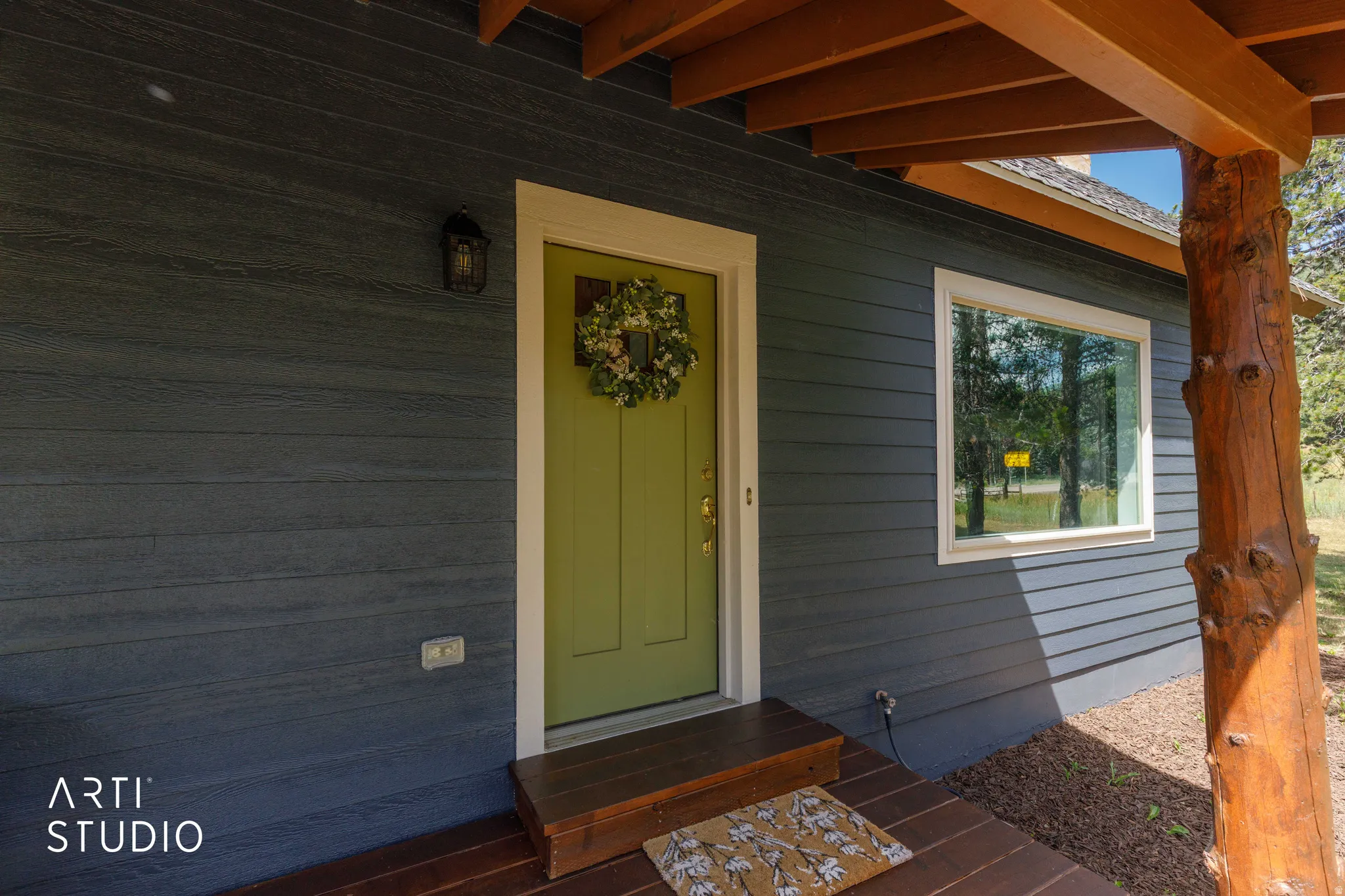 Dark gray horizontal siding, light green entry door with white trim, a single pane window, and a natural wood porch column