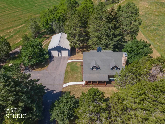 Expansive property featuring a main residence with a covered porch and dormer windows, a detached two-car garage, mature trees, and a paved driveway
