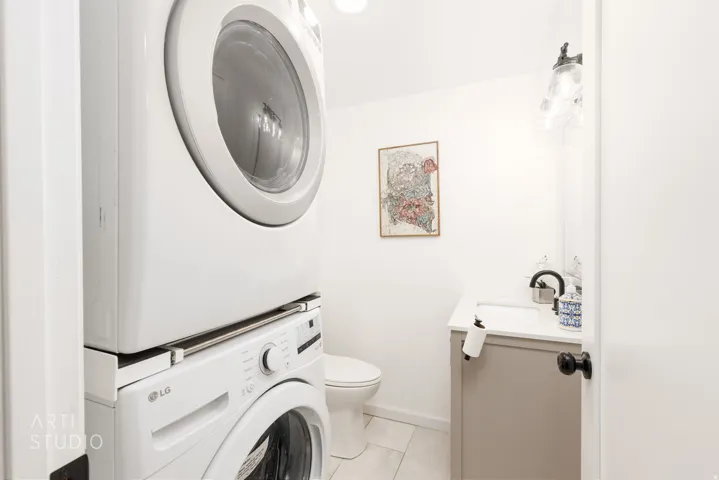 Stackable washer and dryer, vanity with a white countertop, wall-mounted light fixture, and toilet