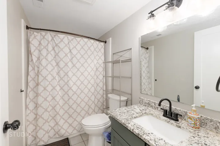 Bathroom featuring a vanity with a white rectangular sink, granite-style countertop, matte black faucet, and a wall-mounted mirror with an overhead light fixture