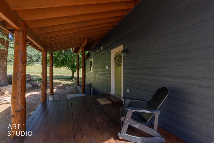 Covered wood deck with natural wood support posts, dark horizontal exterior siding, and a light-colored entry door with an overhead light fixture