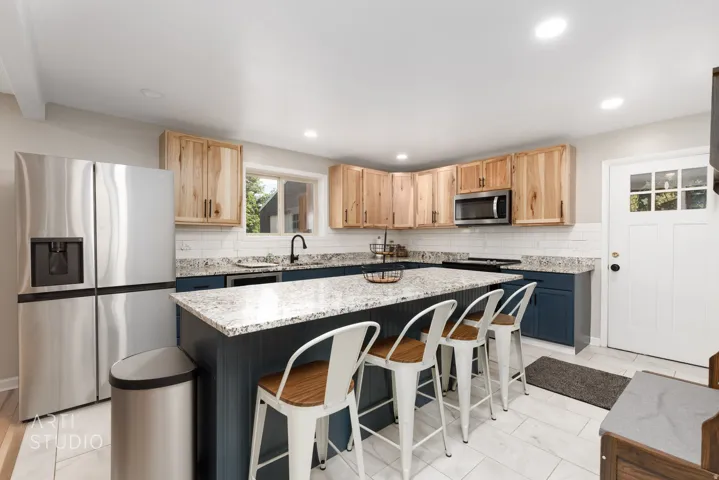 Kitchen featuring a large island with a stone-finish countertop, light wood-finish cabinetry, stainless steel appliances, a white subway tile backsplash, and light tile flooring