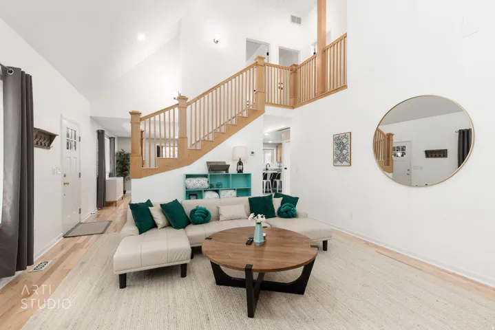 Vaulted ceilings with recessed lighting, light wood-finish flooring, natural wood staircase with balusters, and a split-pane entry door