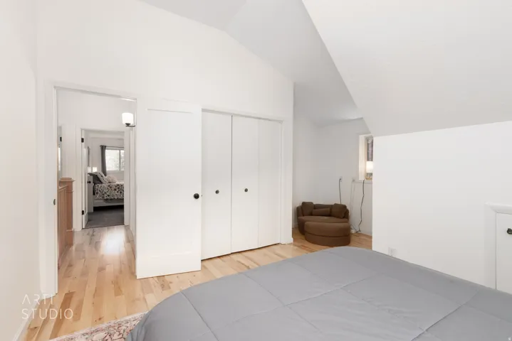 Vaulted ceiling with a white finish, light wood-finish flooring, and white bi-fold closet doors