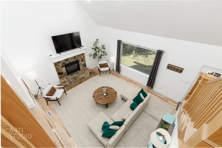 Vaulted ceiling, stone surround fireplace with white mantel, light wood-finish flooring, large picture window, and wood slat open staircase