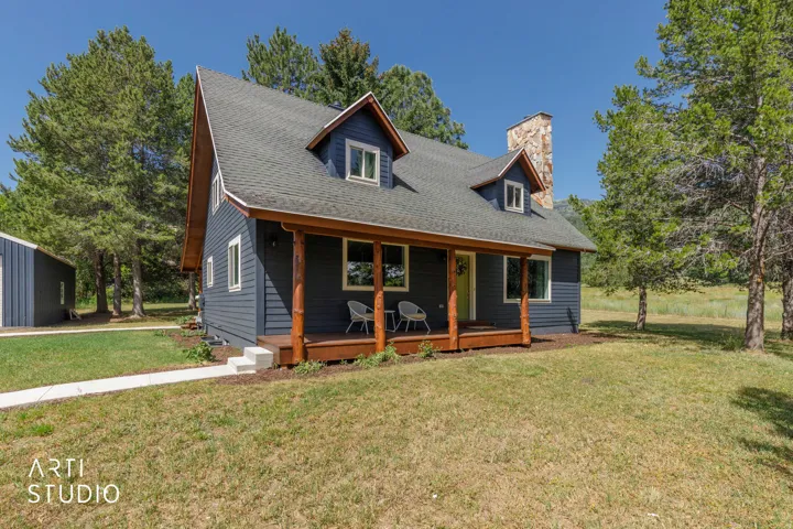 Blue siding exterior with dormer windows, stone chimney, wood-finish porch, and a detached building