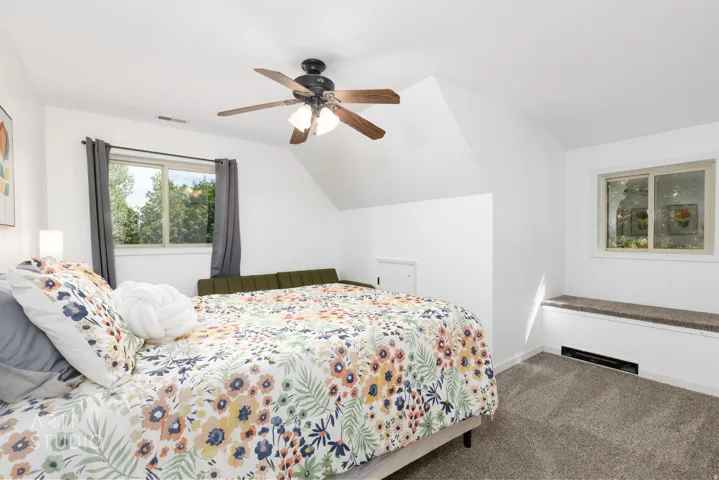 Carpeted flooring, sloped ceiling, ceiling fan with light fixture, window with outdoor scenery, built-in window bench