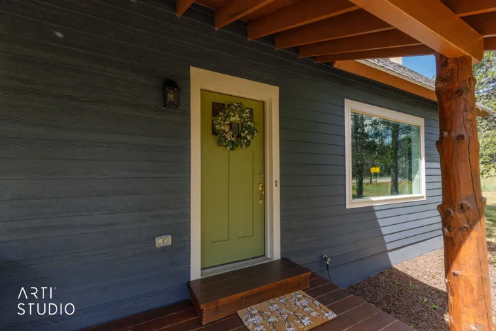 Dark gray horizontal siding, light green entry door with white trim, a single pane window, and a natural wood porch column