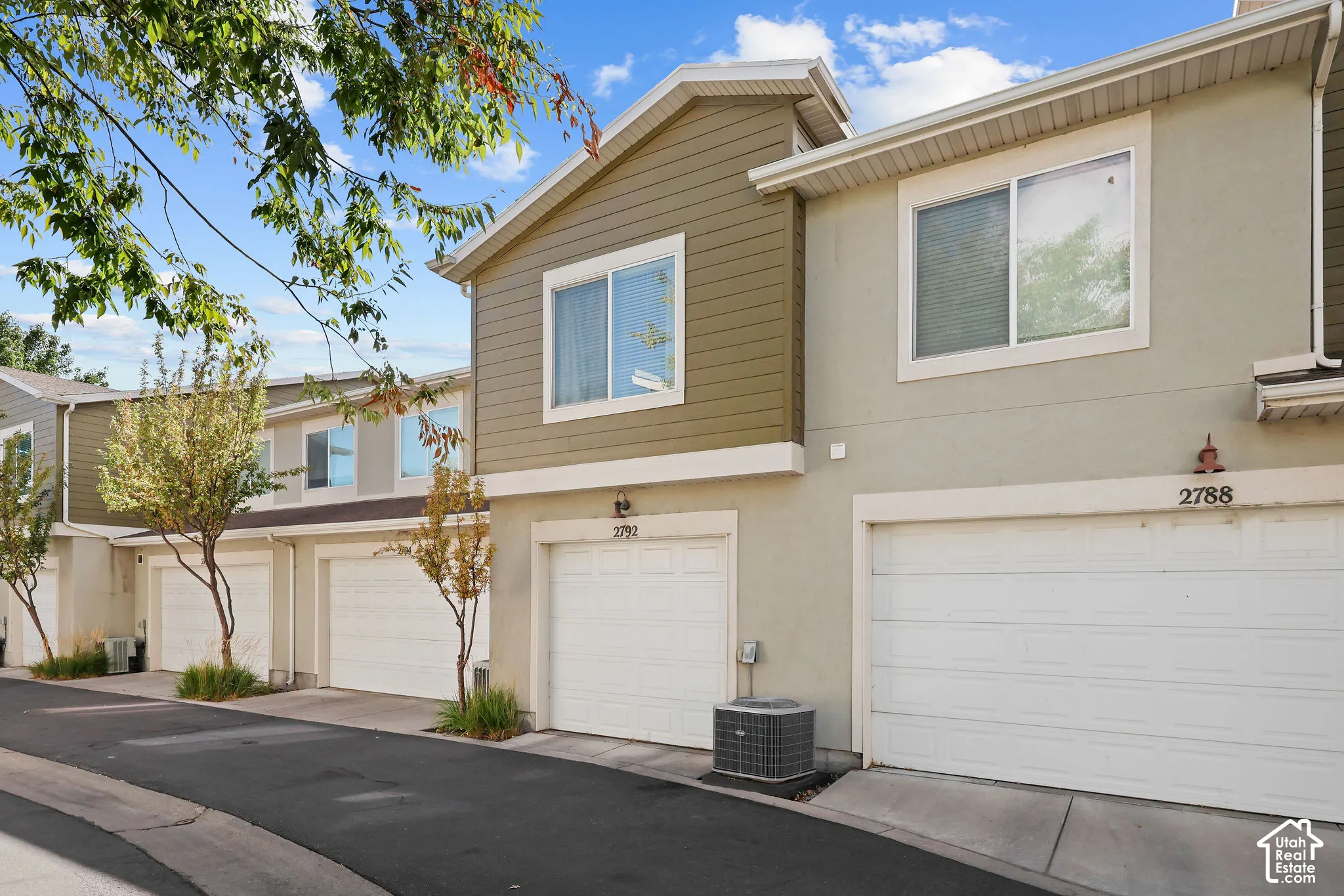 Stucco exterior with horizontal siding accents, individual garage doors, and mature trees lining the driveway