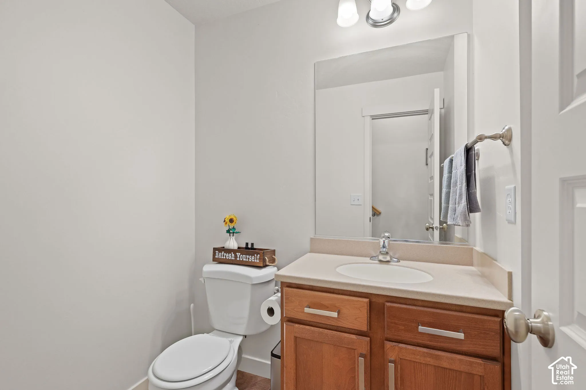 Light-toned countertop with integrated sink, wood-finish vanity with panel doors and drawer, brushed nickel faucet, mirror, and wall-mounted vanity lighting