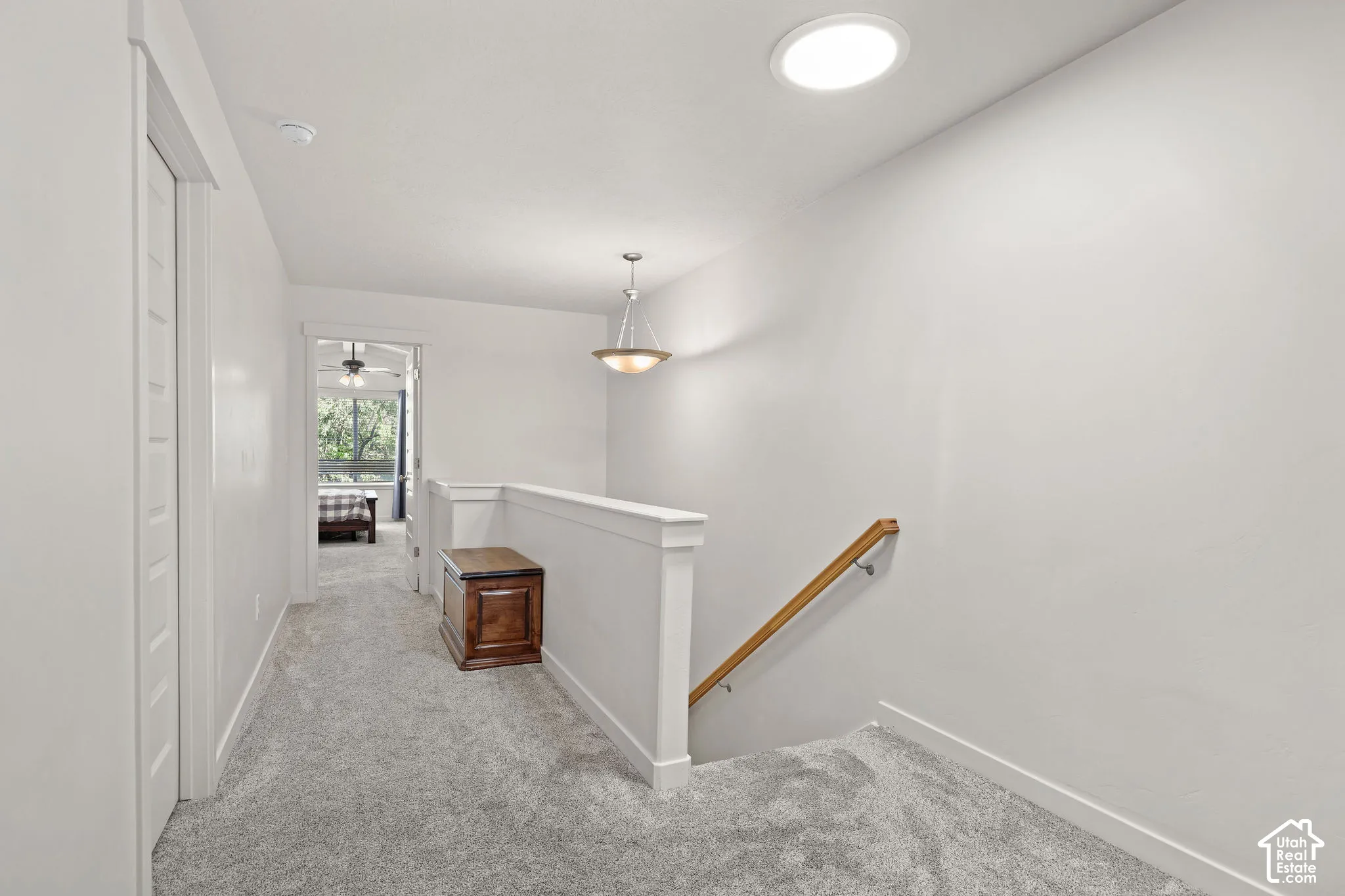 Carpeted hallway with white walls, white trim, and a white balustrade with a wood handrail