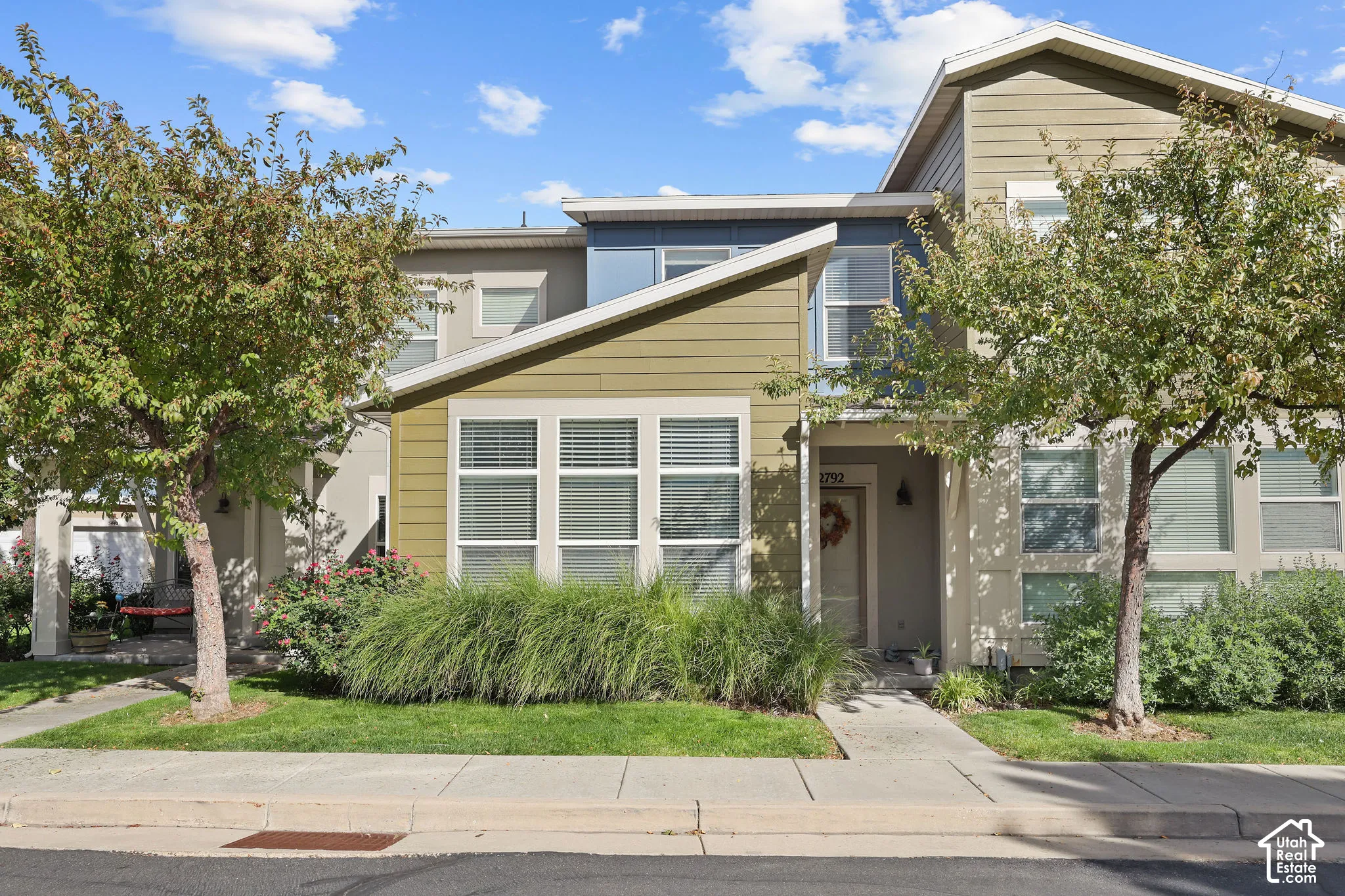 Multi-level exterior with mixed siding, multiple windows, established trees, and a concrete walkway