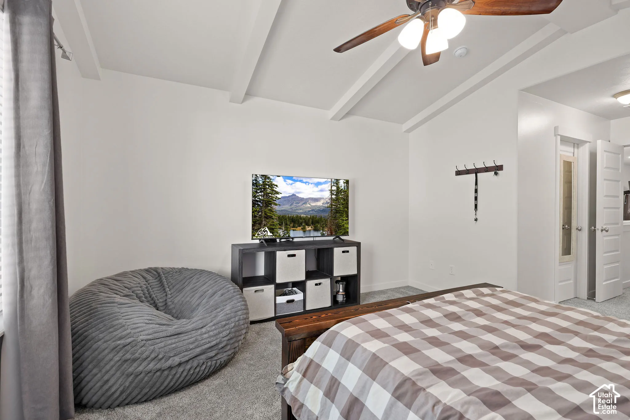 Vaulted ceiling with exposed beams, ceiling fan light fixture, and light gray carpeting