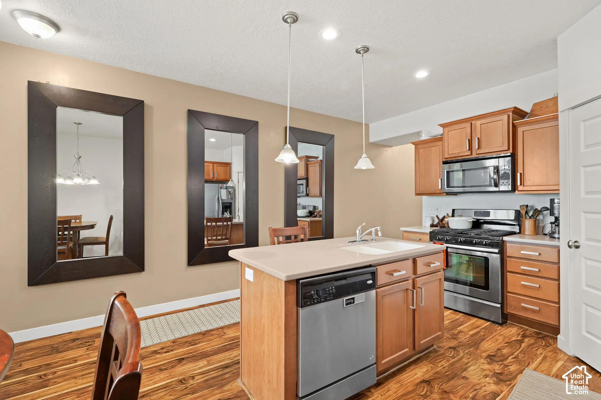 Kitchen with wood-finish flooring, light wood cabinetry, stainless steel appliances, and a central island with a sink and dishwasher
