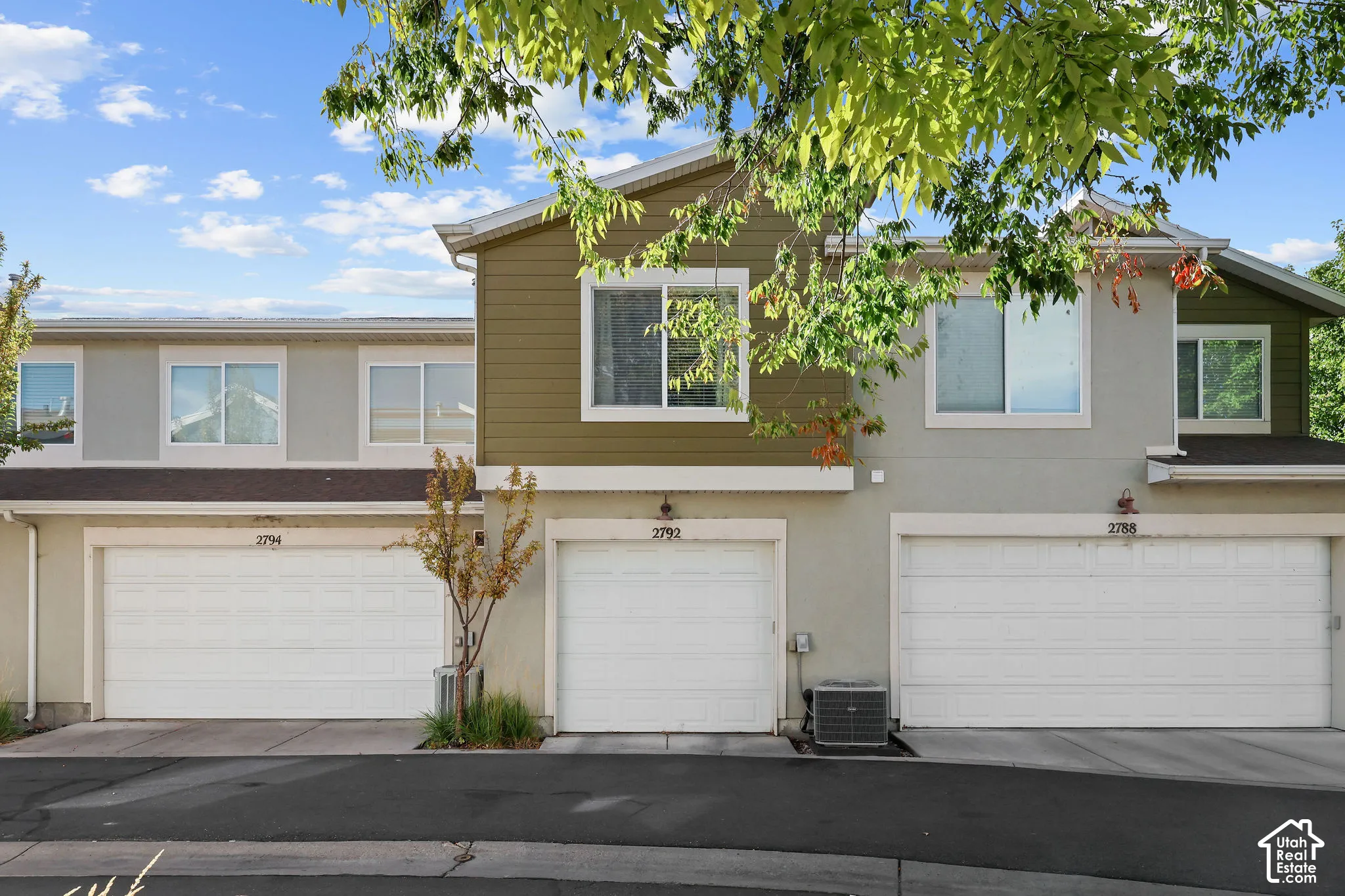 Multi-level townhouse exterior with contrasting siding, prominent garage doors, and mature foliage