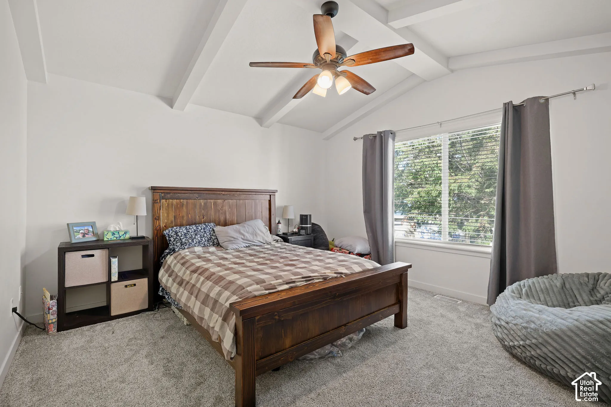Vaulted ceiling with exposed beams, ceiling fan, carpeted flooring, and a large window