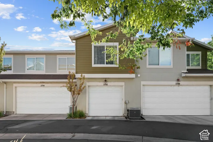 Multi-level townhouse exterior with contrasting siding, prominent garage doors, and mature foliage